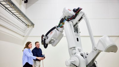 Two engineers programming a large, white ABB industrial robot arm in a lab environment.